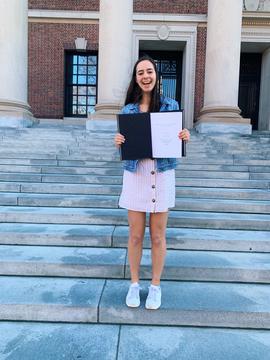 Abigail Simon smiling and holding her completed thesis